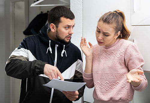 Man pointing to a document while explaining a credit issue to a confused woman indoors.